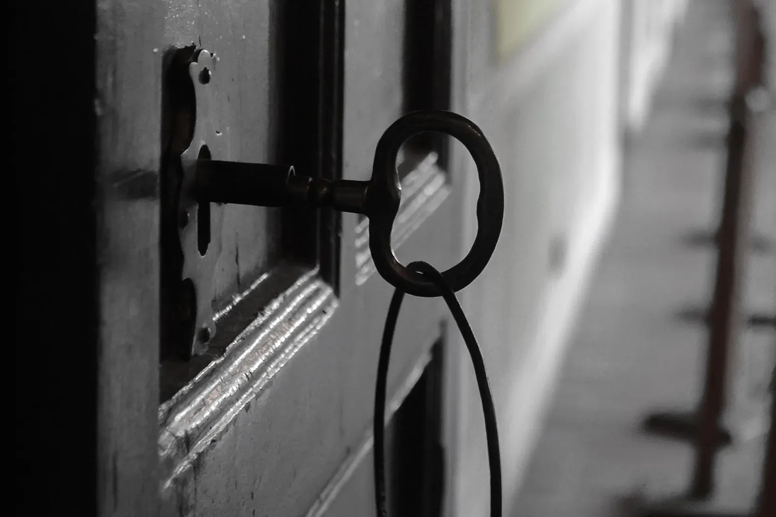 An old iron key with a round bow sitting in the lock of a dark wooden door