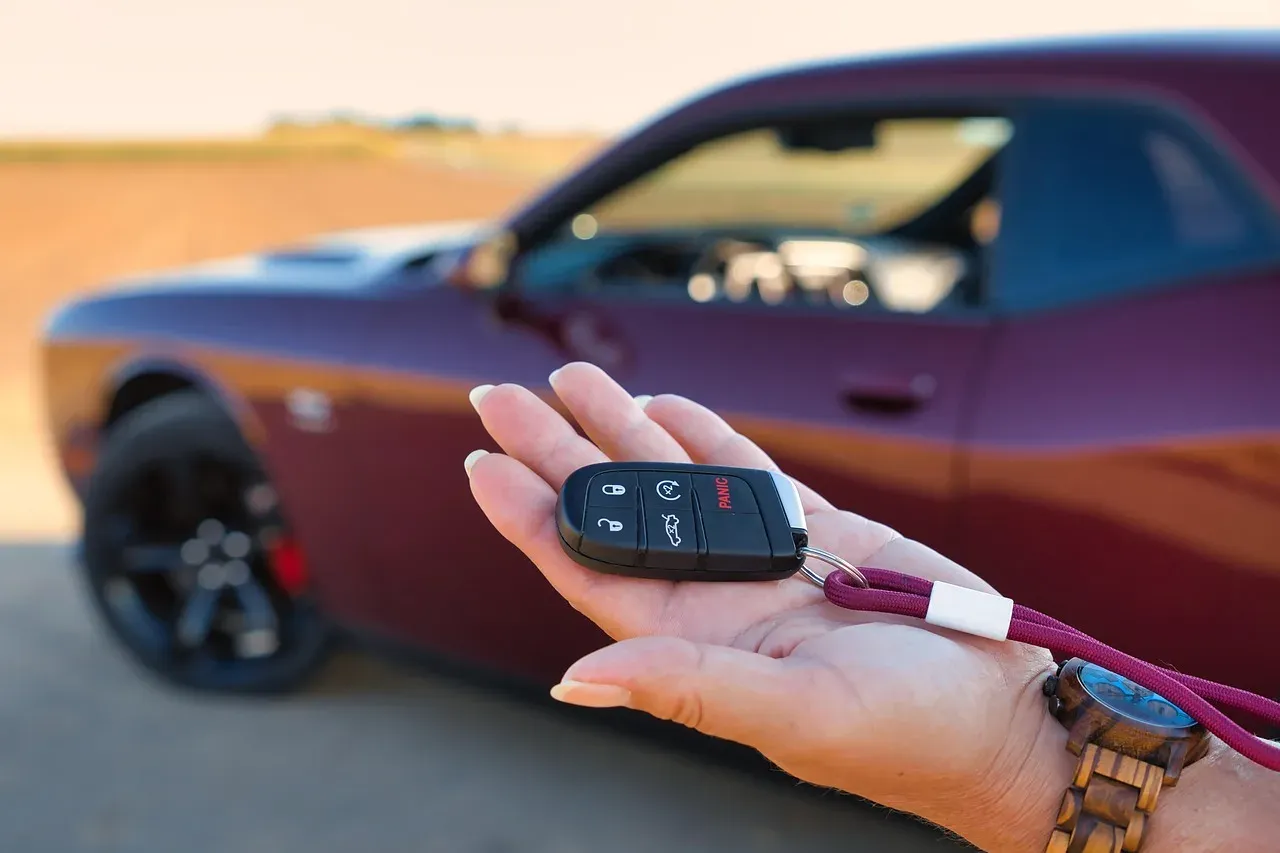 A hand holding a black key fob out in front of a parked car