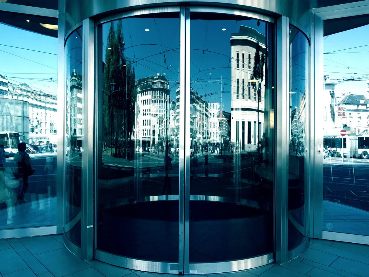 A curved glass revolving door entrance to a building, reflecting the street outside