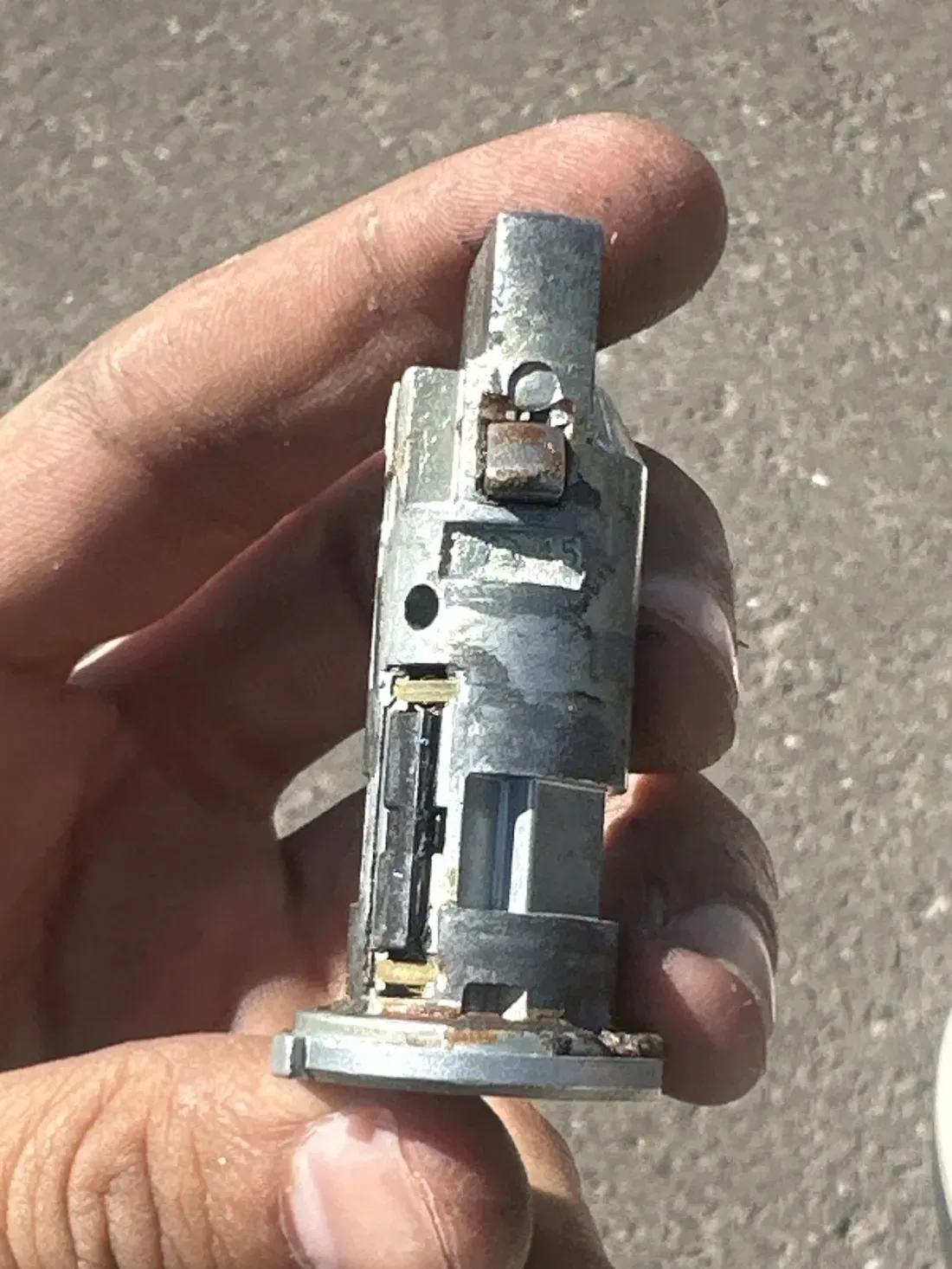 A worn metal lock cylinder held in a hand, showing its internal wafers and wear